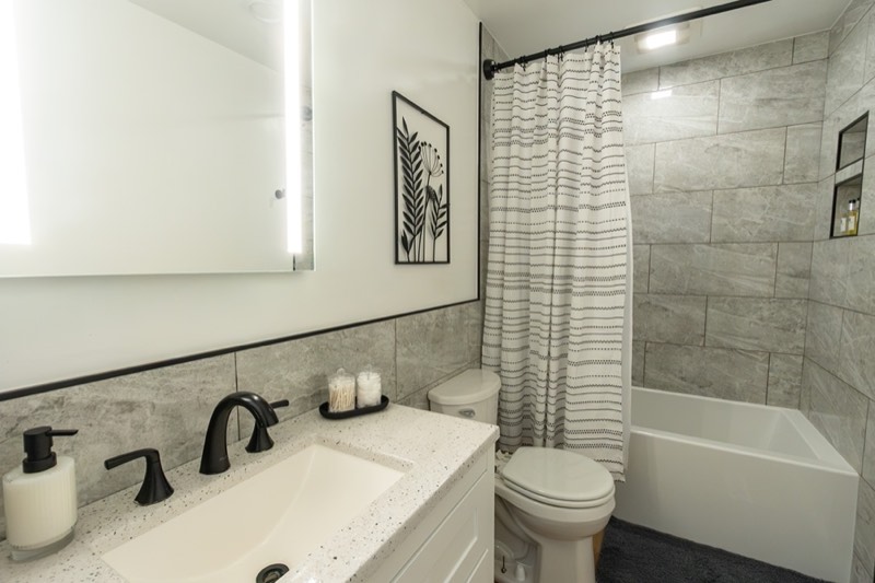 Upstairs bathroom with a tub and shower, gray tile, and a lit mirror